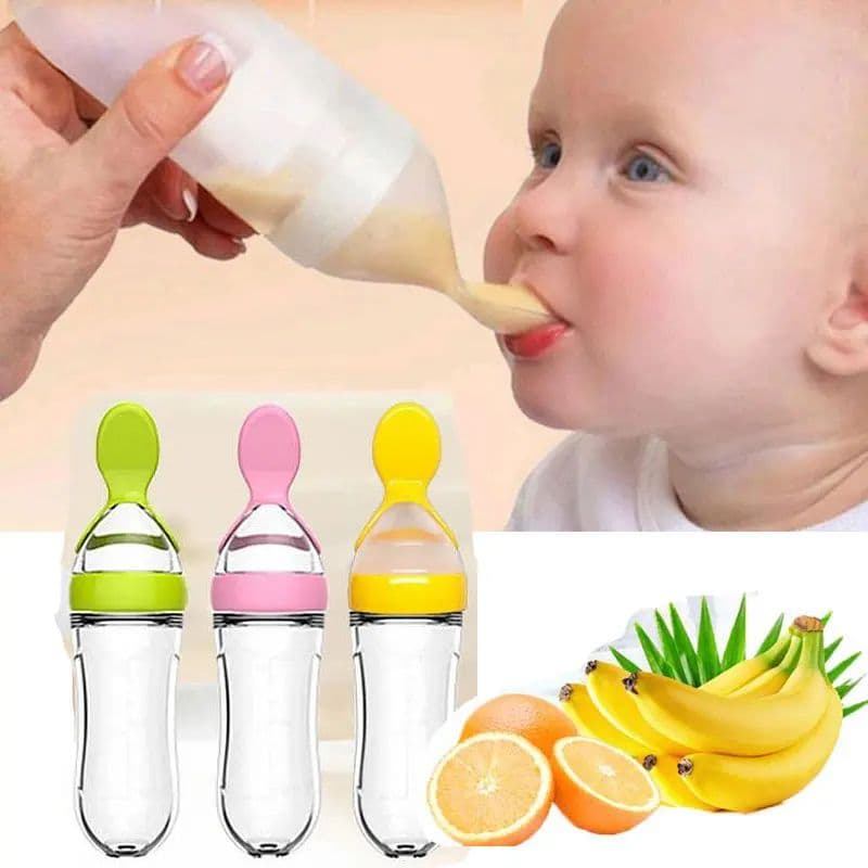 An adult feeding a baby puree from a clear squeeze bottle spoon feeder alongside green, pink, and yellow spoon feeders.
