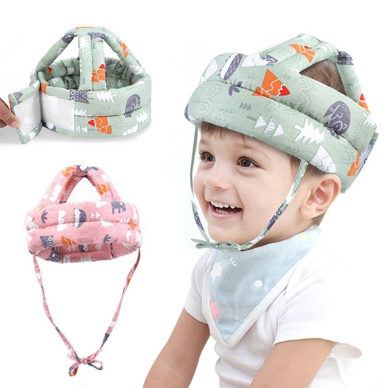 A toddler wearing a soft patterned green protective helmet with chin ties, next to detailed views of the helmet strap and a pink option.