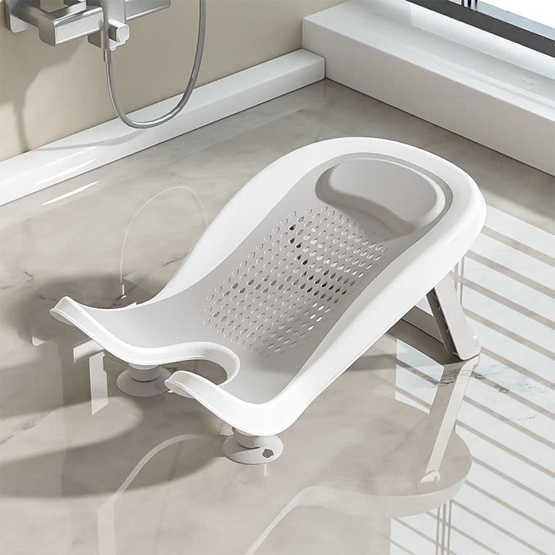 White inclined baby bath seat featuring a grey perforated mesh resting surface, integrated headrest, and suction cup feet.