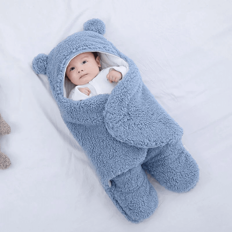 A baby wrapped in a light blue textured teddy fleece swaddle with bear ears on the hood.
