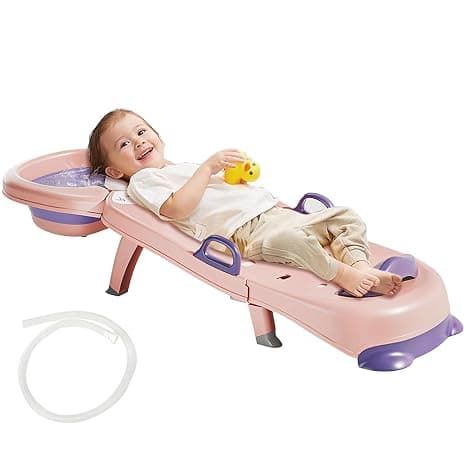 A toddler laying back comfortably on a pink and purple reclined kids hair washing chair equipped with a head basin.