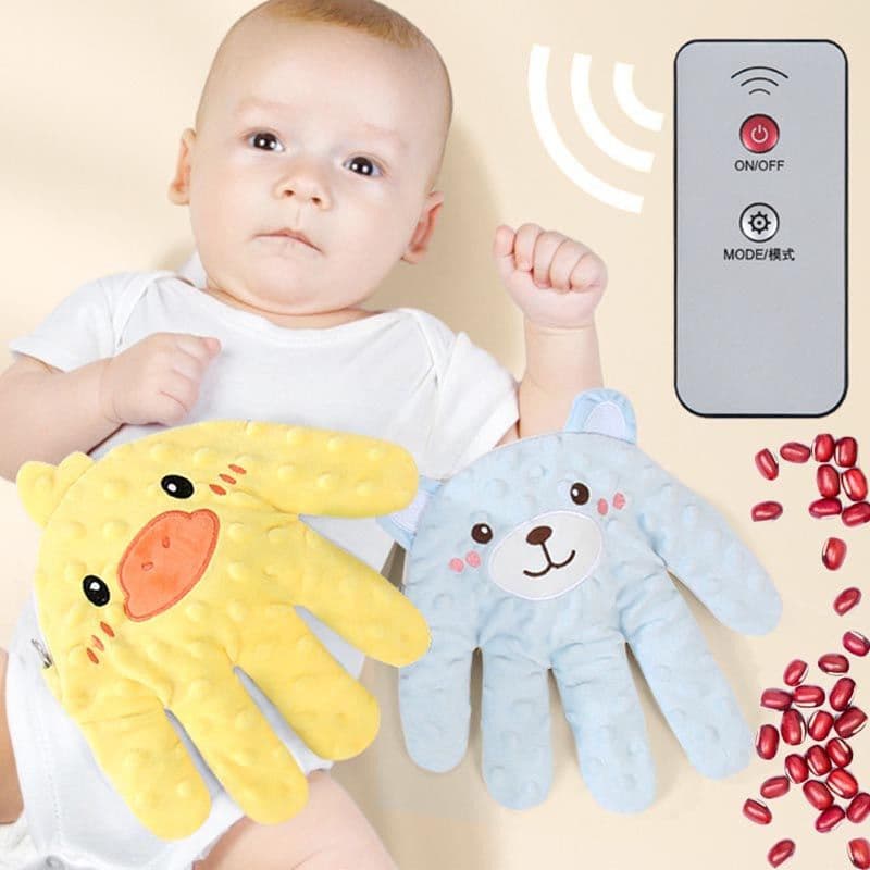 A baby lying on a light surface with yellow duck and blue bear hand-shaped plush pads alongside a remote control.